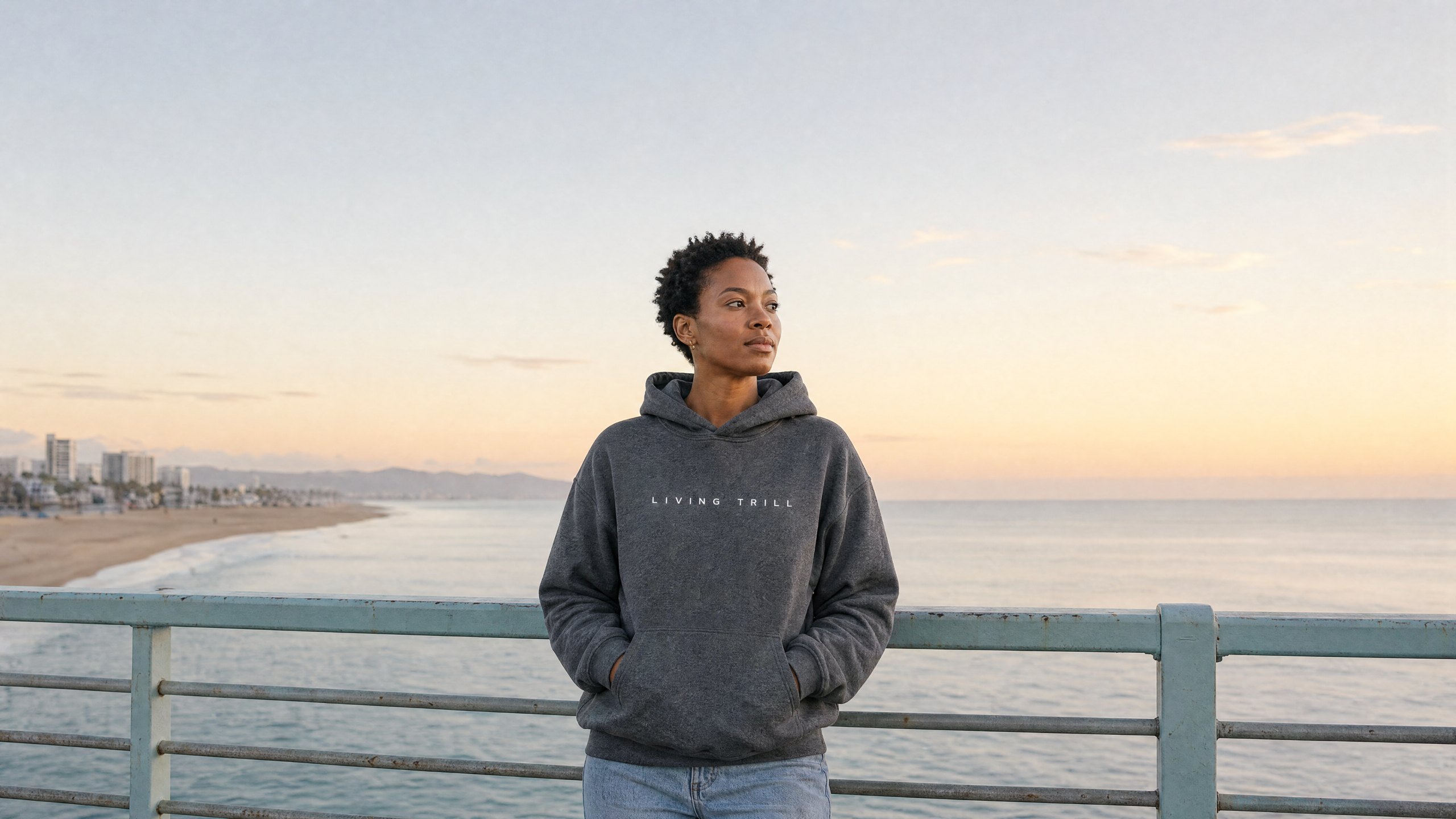 Living Trill — woman in the LIVING TRILL hoodie at dawn on an empty boardwalk above the ocean